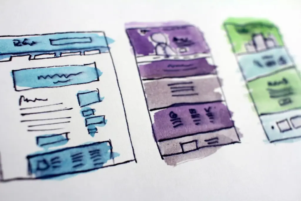 Hand-drawn website wireframes with colored markers, depicting three different layout designs divided into sections.